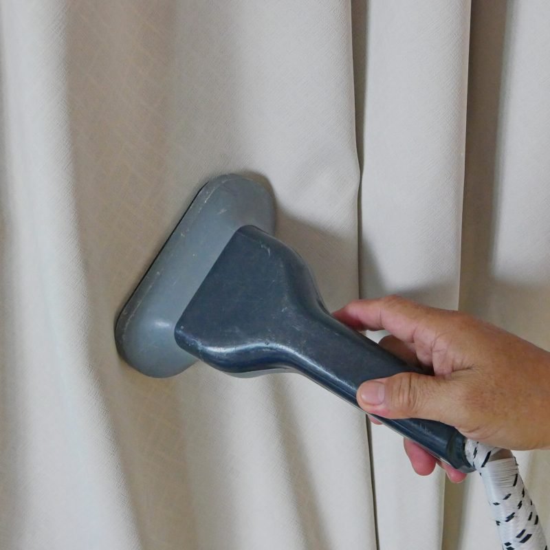 A hand of a man holding on a garment steam head while doing a steam clean for house curtains